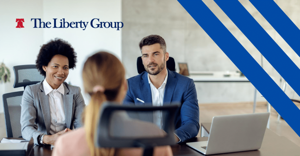 Two diverse professionals interview a temporary staff applicant with The Liberty Group logo at the top left corner.