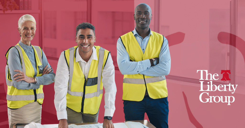Three people in yellow safety vests stand smiling in an office; The Liberty Group logo is on the right.