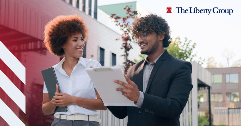 Two property management professionals holding a clipboard and folder outdoors; The Liberty Group logo is at the top right corner.