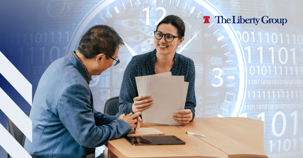 Two people sit at a table during an interview with a background that features a clock and binary code; The Liberty Group logo is at the top right corner.
