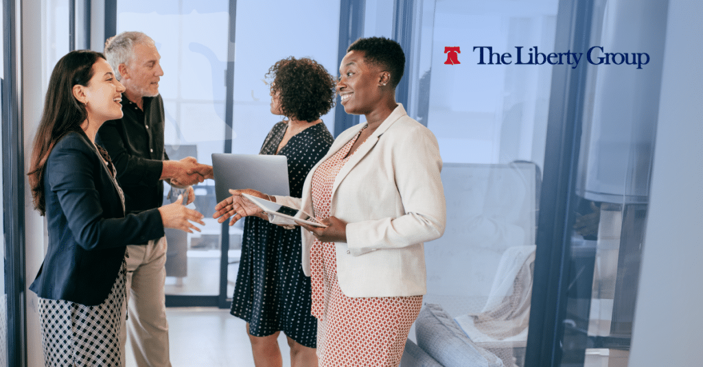 Business professionals meeting and collaborating in an office with The Liberty Group logo in the background.
