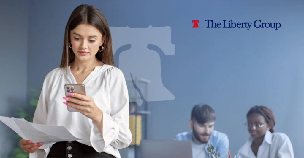 Job candidate reviews resume and phone before applying for a real estate job, with The Liberty Group logo in the background.