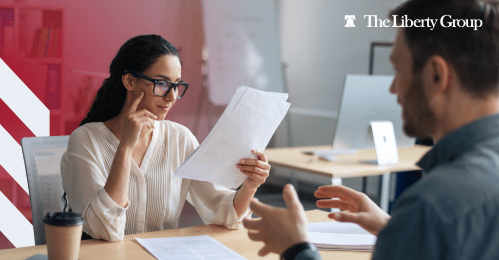 Two professionals reviewing documents together in an office setting with The Liberty Group logo in the corner.